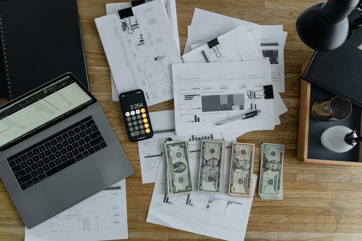 aerial view of a laptop, a calculator, bank notes, and accounting documents on a wooden desk