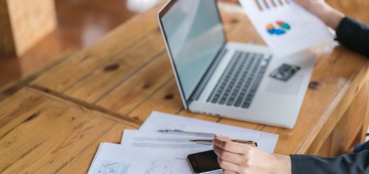 business woman holding a financial chart and a pen while working on a laptop