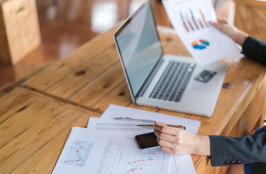 business woman holding a financial chart and a pen while working on a laptop