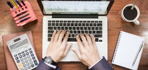 aerial view of a businessman typing on a laptop, with a calculator and notebook next to it