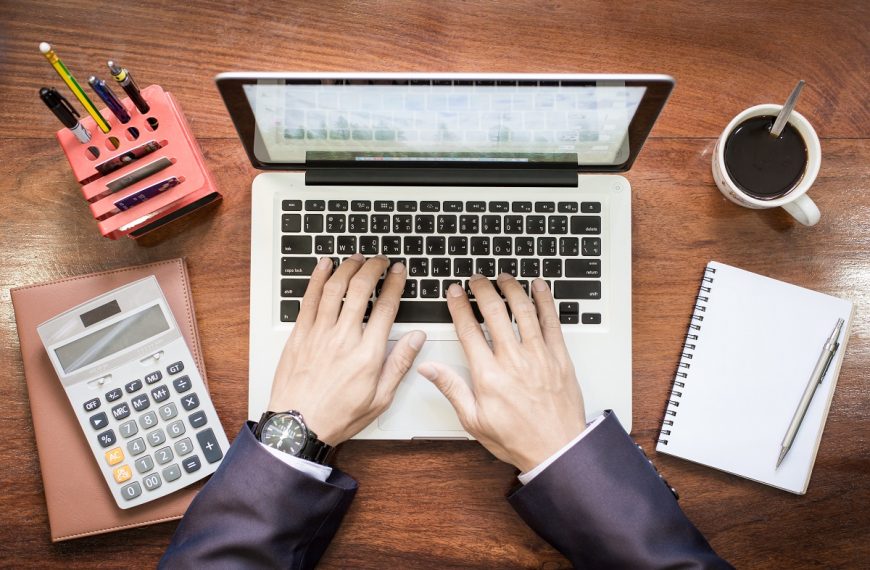 aerial view of a businessman typing on a laptop, with a calculator and notebook next to it