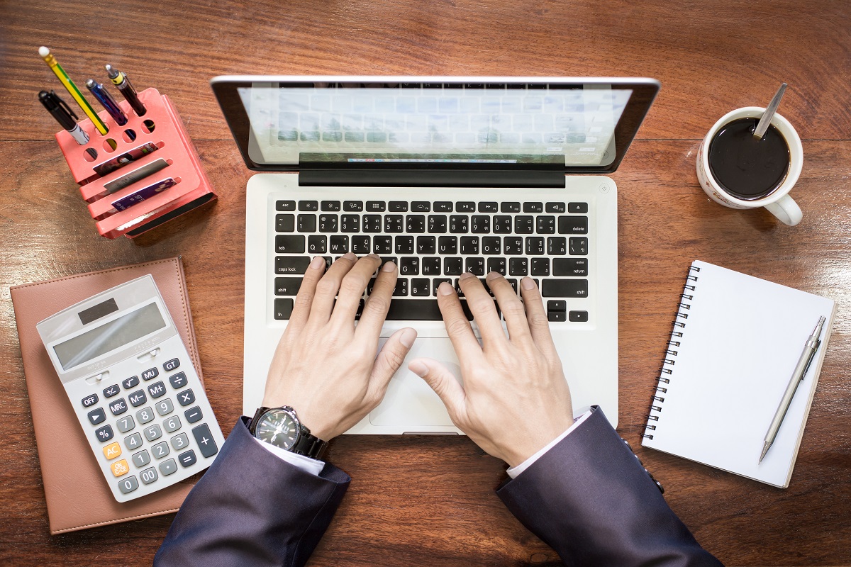 aerial view of a businessman typing on a laptop, with a calculator and notebook next to it