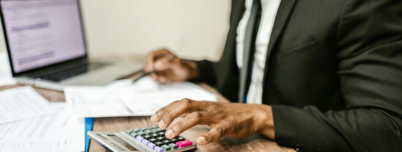 man in a suit working at a desk with a laptop, papers, and a calculator