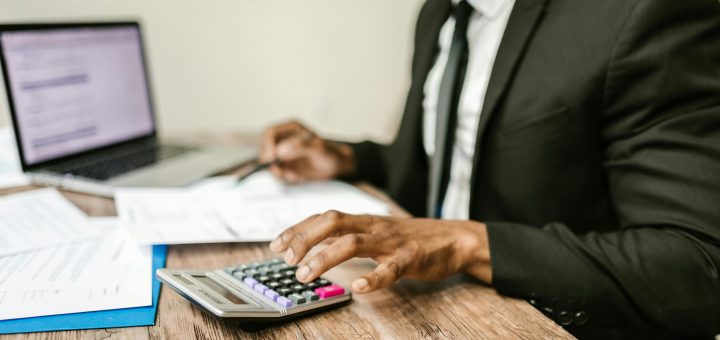 man in a suit working at a desk with a laptop, papers, and a calculator